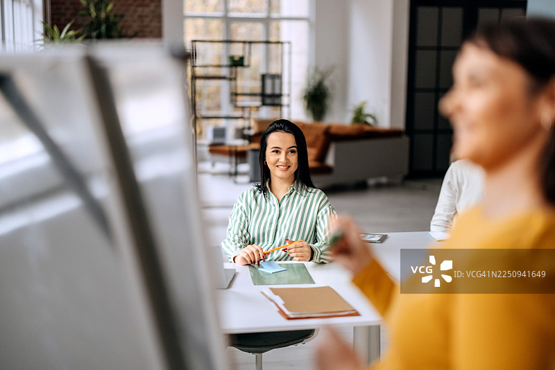 年轻女子在办公室参加团队会议，面带微笑图片素材