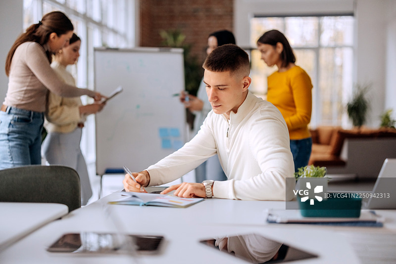 年轻男子在办公室的团队会议中做笔记图片素材