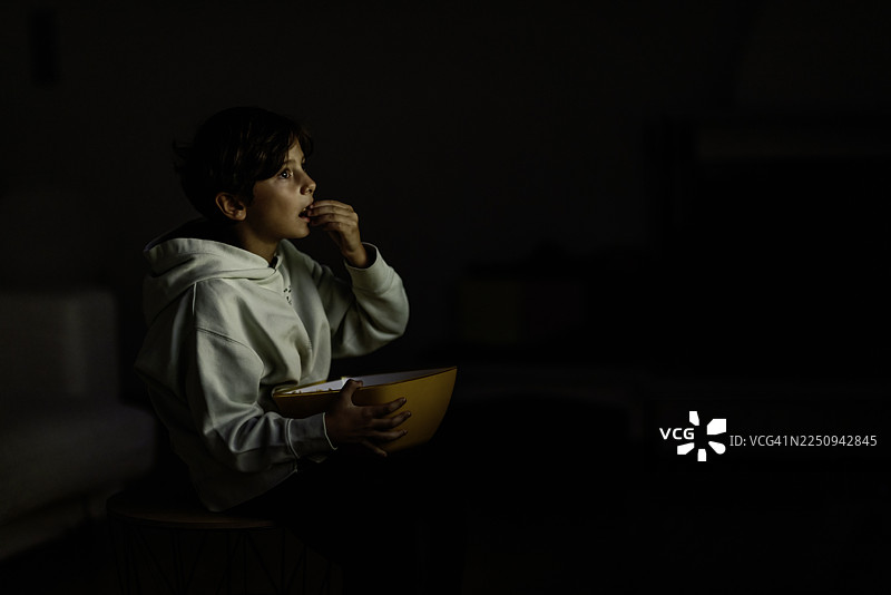孩子晚上在家一边看电影一边享受零食图片素材