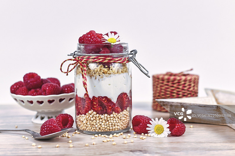 罐子里的健康树莓水果甜点，包含斯凯尔酸奶、格兰诺拉麦片和膨化藜麦谷物，周围摆放着配料。图片素材