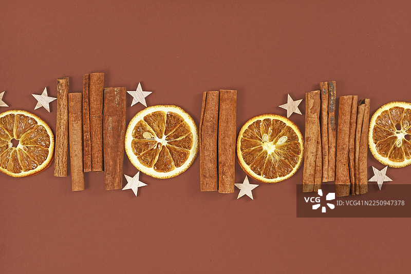 一排排季节性的天然干橙片、肉桂棒和星星装饰品摆放在棕色背景上图片素材