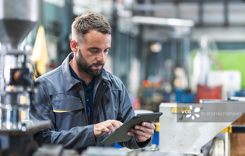 技术人员在工厂进行日常工作，检查塑料注塑机的控制面板。图片素材