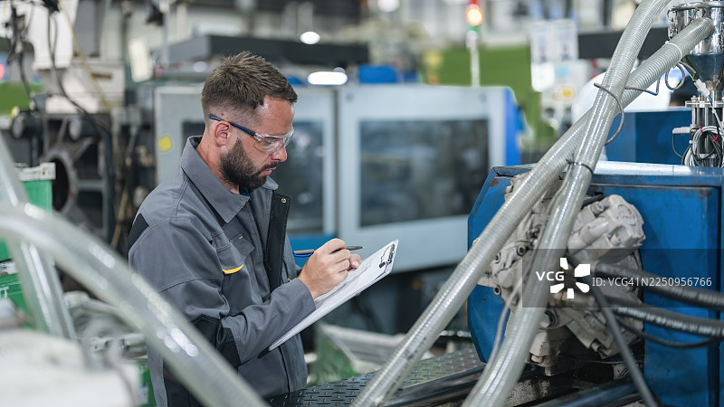 男性技术人员在工厂工作，进行塑料注塑机的控制面板的日常例行视觉检查。图片素材