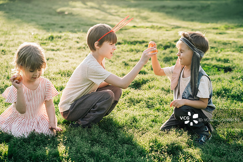 阳光明媚的春天，孩子们在田野里手持彩蛋，准备互相敲击。图片素材
