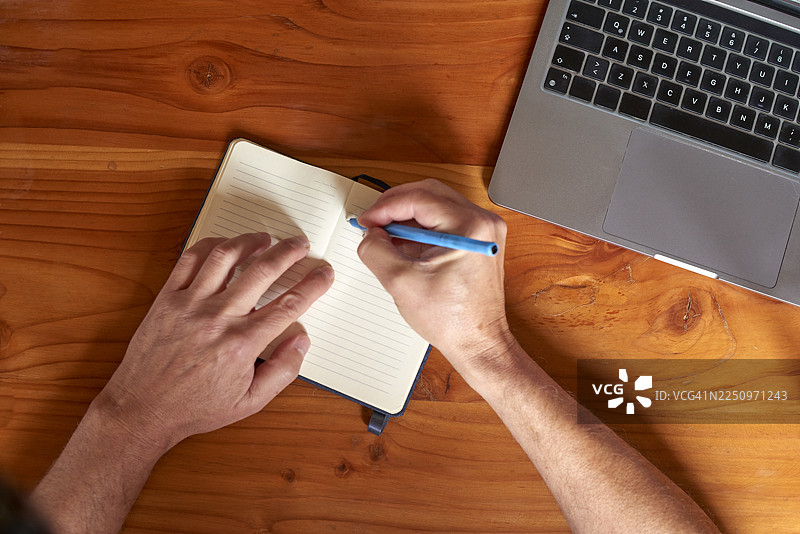 一个人正在木制办公桌上用笔记本电脑写字图片素材