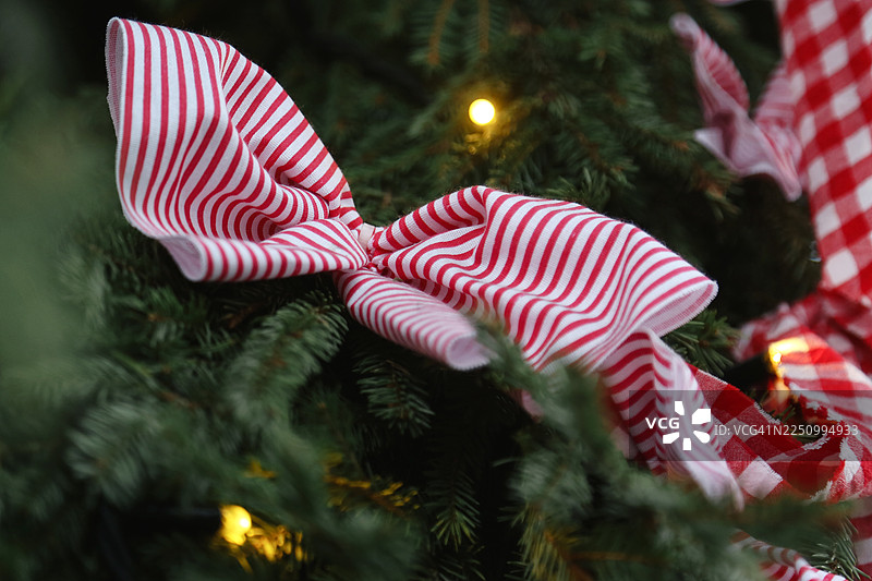 圣诞树上装饰着手工制作的红白条纹棉带和蝴蝶结，背景是发光的彩灯。图片素材