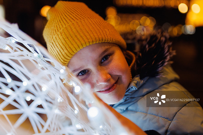 戴着黄色针织帽的小女孩在夜晚欣赏着温暖发光的串灯图片素材