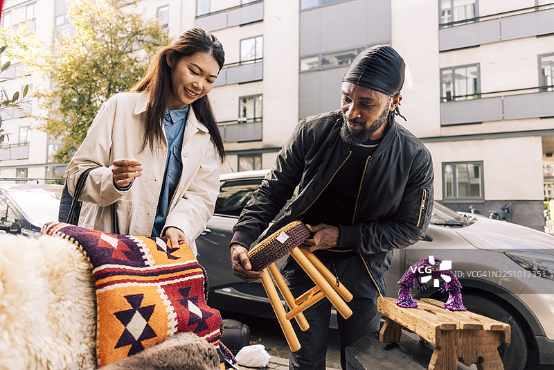 男人抱着凳子，站在一位朋友旁边，她正在旧货店购买被子图片素材