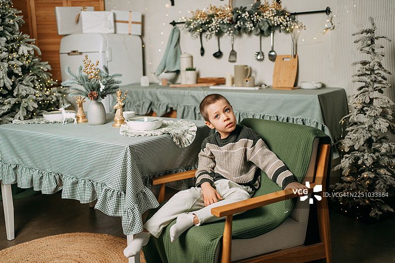 患有自闭症的小男孩在家中圣诞装饰的厨房里坐着图片素材