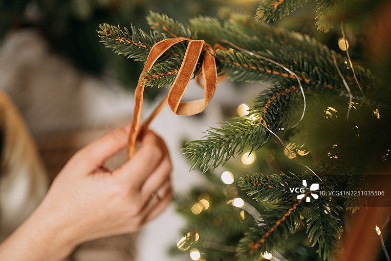 一个人在节日庆典期间用丝带装饰圣诞树图片素材