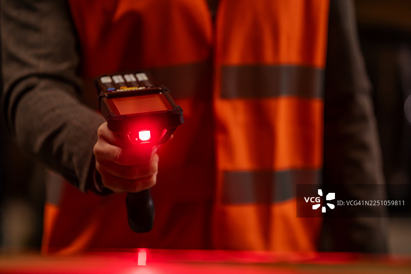 近距离拍摄正在工作的条形码扫描仪，背景中有一位身穿安全背心的工人图片素材