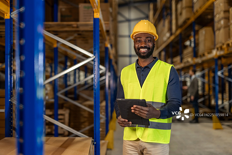 微笑的仓库工人手持平板电脑在仓库内图片素材