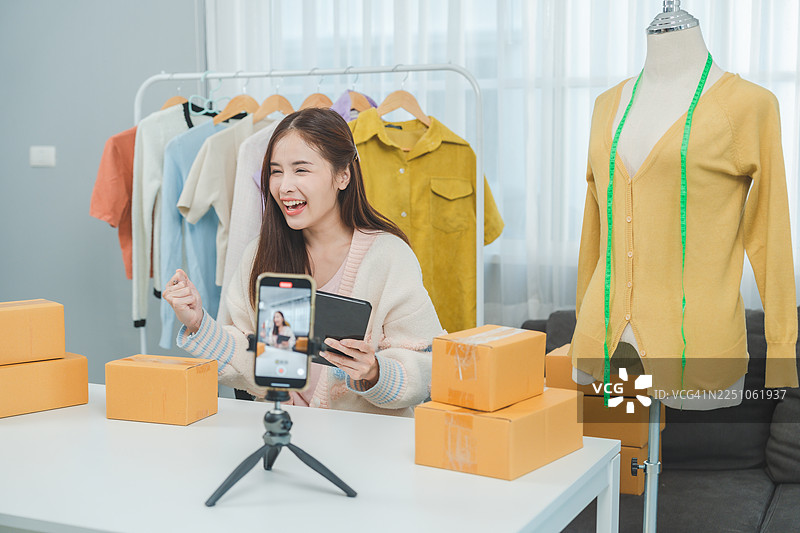 年轻的女企业家正在她的家庭工作室录制时尚直播销售视频，高效地展示服装和打包订单。图片素材