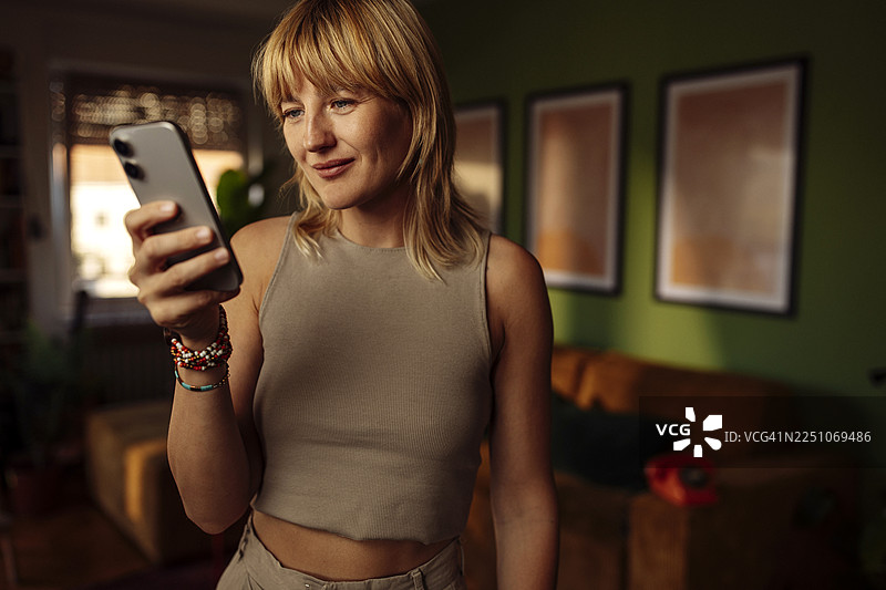 家中使用智能手机的女性，在温暖的光线下图片素材