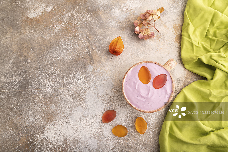 紫色的酸奶，上面放着果冻糖，背景是棕色的混凝土和绿色的纺织品，俯视，平面图，留白，极简主义图片素材