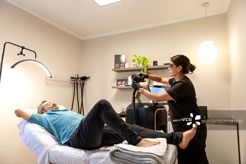 皮肤科医生正在为男性患者进行激光治疗，以对抗灰指甲。图片素材