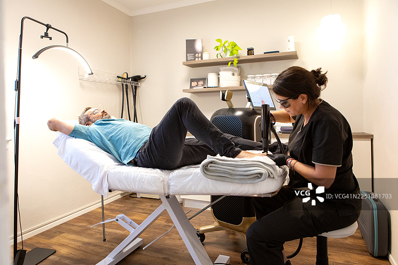 皮肤科医生正在为一名男性患者进行激光治疗，以对抗灰指甲。图片素材