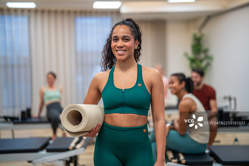 一位微笑的西班牙裔女性在普拉提工作室手持瑜伽垫图片素材