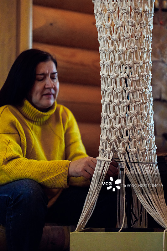 女子坐在室内，穿着黄色毛衣，编织着绳编挂毯图片素材