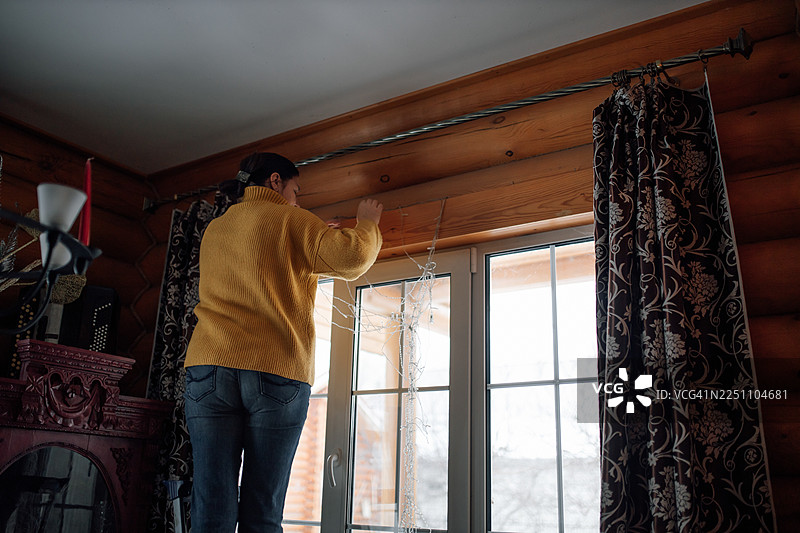 一位女士正在温馨的木屋里用串灯装饰窗户图片素材
