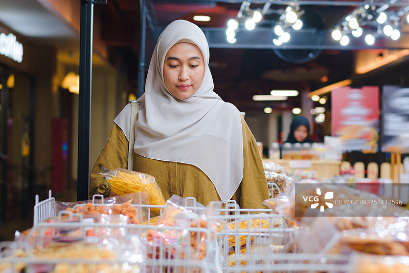 印尼女性戴着头巾在零售店挑选传统棒状零食图片素材