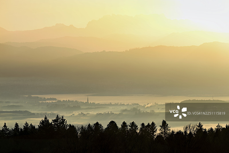 从霍本眺望楚格湖，湖边的楚格市和楚格市被雾笼罩，后面是瑞吉山和弗伦里斯加特利山，在初升的太阳光下，位于瑞士阿尔高州拜因维尔-弗莱阿姆特。图片素材