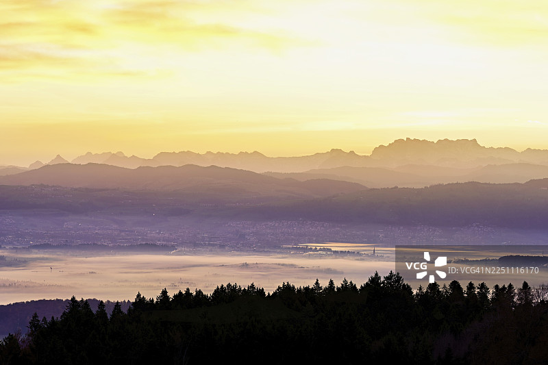 从霍本眺望楚格湖，卡姆市和楚格市笼罩在雾中，其后是初升阳光下的雪山弗吕布里格和弗雷内利斯加特利，位于瑞士阿尔高州拜因维尔-弗莱阿姆特。图片素材
