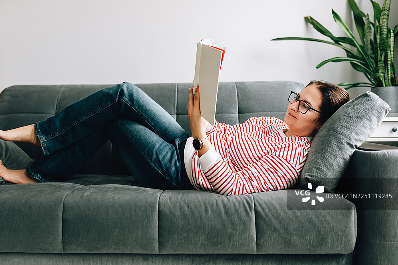 女人在家中舒适地躺在沙发上读书图片素材