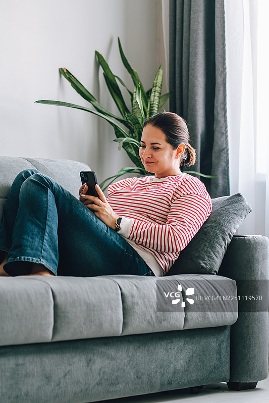 一个女人在家躺在沙发上玩手机图片素材
