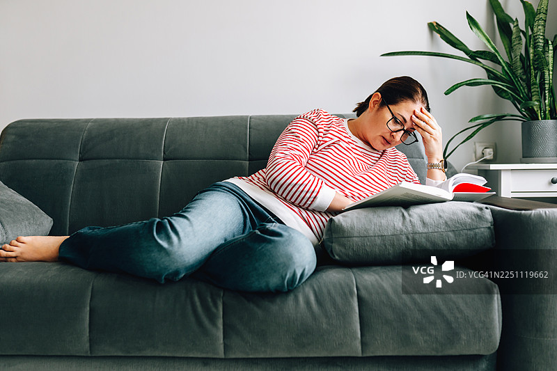 女人在沙发上阅读时感到压力和疲惫图片素材