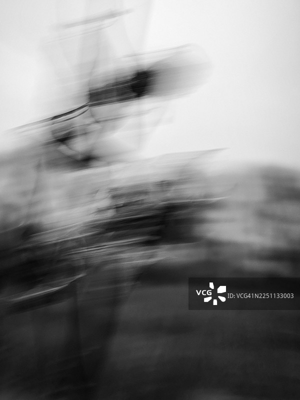 抽象的模糊场景，通过刻意的相机移动创作而成，展示了干枯植物被拉伸的深色形态，背景是苍白的阴天和柔和的草地图片素材