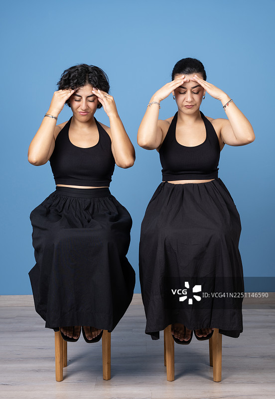两位女士坐着，手按额头，表现出疲惫和头痛图片素材