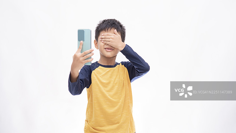 亚洲小男孩在白色背景下看恐怖视频时用手捂住眼睛图片素材
