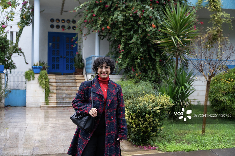 穿着红色高领毛衣的快乐女子站在房子前图片素材