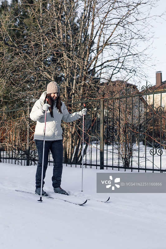 一位年轻女孩在冬日雪景中，在锻铁栅栏旁，手持雪杖滑雪图片素材