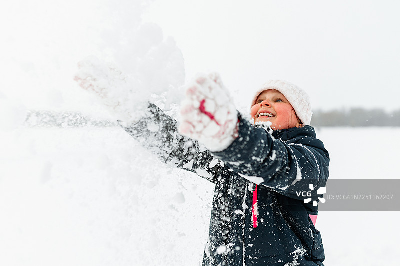 快乐的小女孩在明亮的户外冬日场景中，开心地玩着雪，脸上带着笑容。图片素材