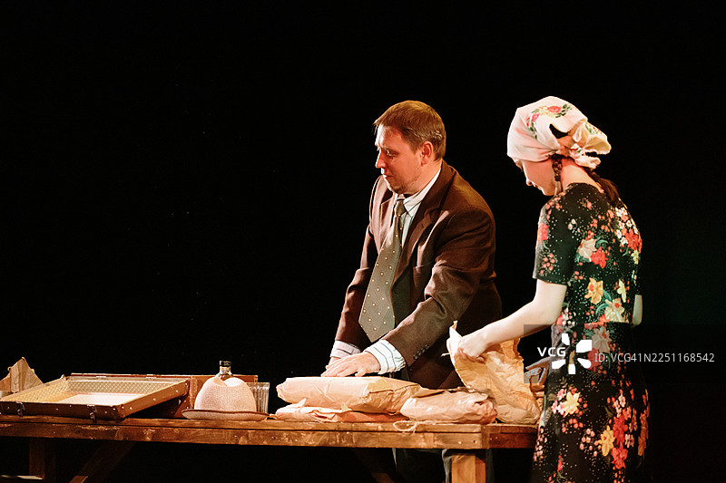 戏剧场景：一男一女在温暖的舞台灯光下围着一张桌子分拣包裹图片素材