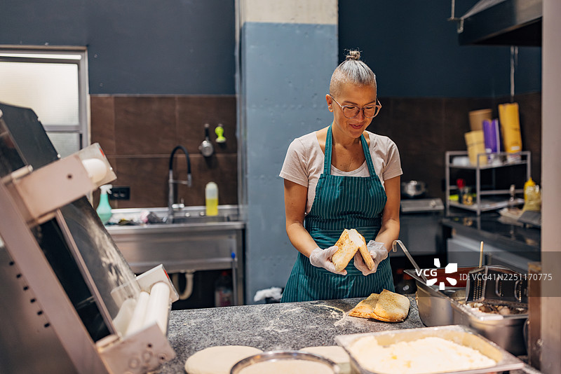 一位穿着围裙的女厨师在商业厨房里准备酿馅意大利饺的正面照图片素材