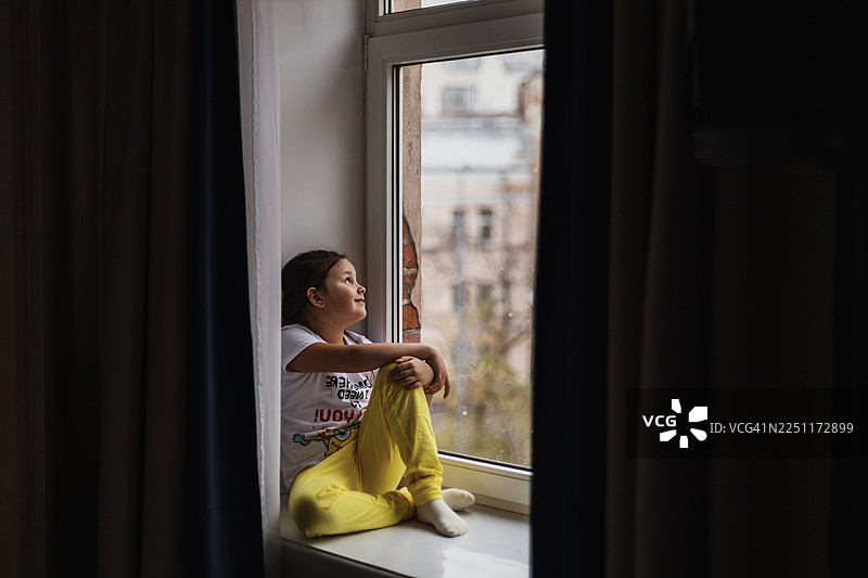 小女孩坐在窗台上，用充满希望和好奇的眼神望着窗外图片素材