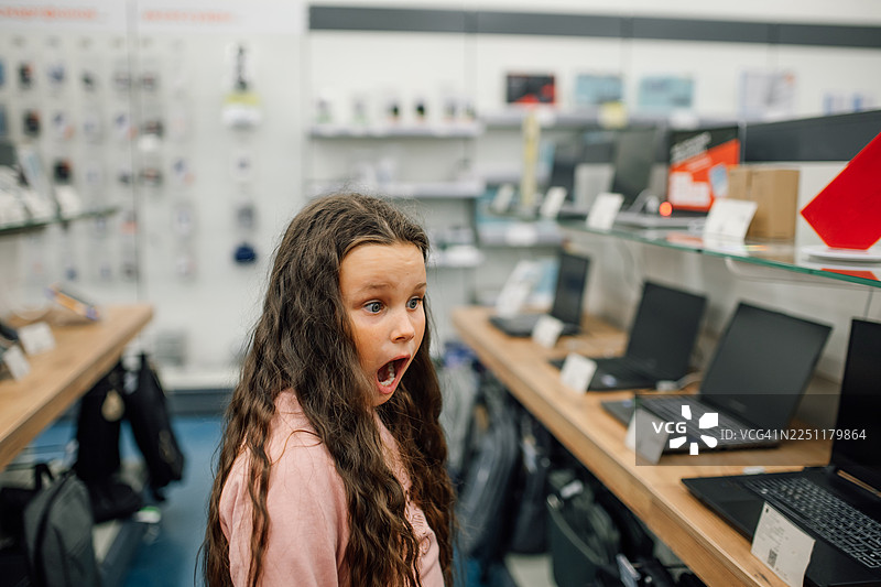 年轻女孩在电子产品商店里，对展示的笔记本电脑感到惊讶图片素材