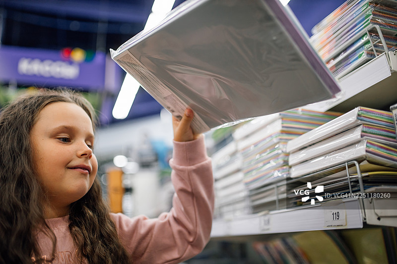 一个小女孩在书店里，从一排五颜六色的杂志架上伸手去拿一本笔记本图片素材