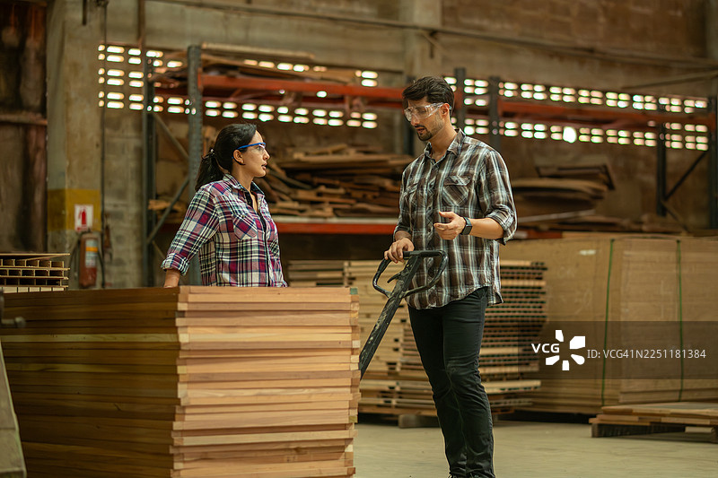 木匠在工业车间里拉动托盘搬运车，上面堆放着木板，展示了制造或木工生产设施的运作，强调力量、效率和亲手操作的工业劳动。图片素材