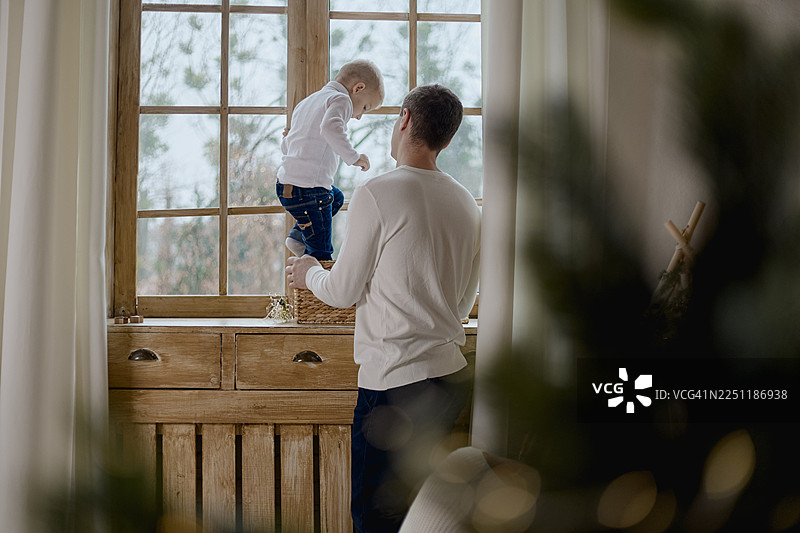 一个金发小男孩在他的父亲的陪伴下，走进一个摆放在木制窗台上的编织盒子。图片素材