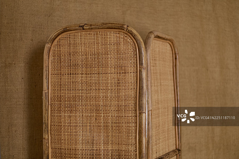 浅棕色藤编房间隔板的两个相邻面板，背景为米色织物。图片素材