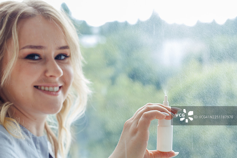 一位女士在雨天的窗边微笑着使用喷雾瓶，传递出清新感和护肤的瞬间图片素材