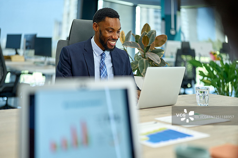 一位非洲裔美国商人，在现代办公室里微笑着使用笔记本电脑工作图片素材