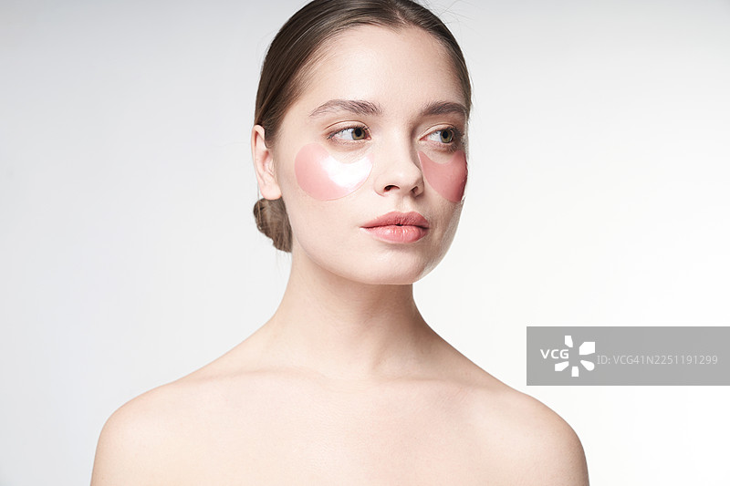 工作室灯光下，一位拥有粉色眼下贴片和洁净肌肤的女性的唯美肖像图片素材