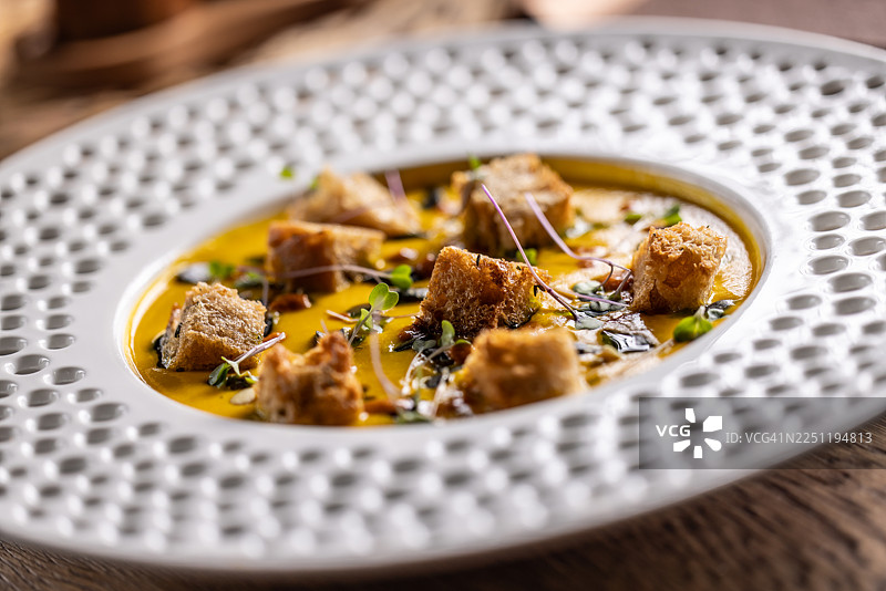 一份摆盘精美的奶油南瓜浓汤，搭配甜辣酱、香脆的酸面包丁和烤南瓜籽。图片素材