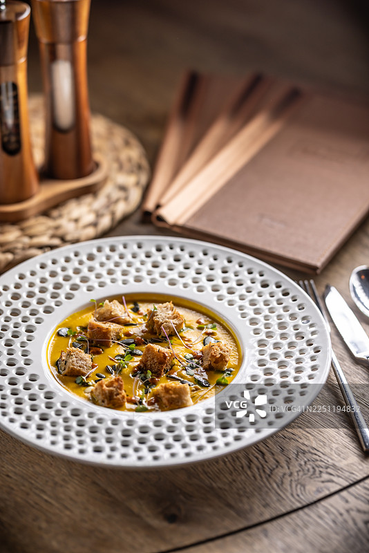 一份精美摆盘的丝滑南瓜奶油，搭配甜辣酱、香脆的酸面包丁和烤南瓜籽。图片素材