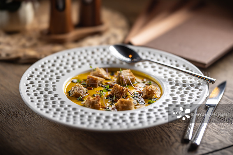 一份精致的南瓜奶油浓汤，配有甜辣酱、酥脆的酸面包丁和烤南瓜籽。图片素材